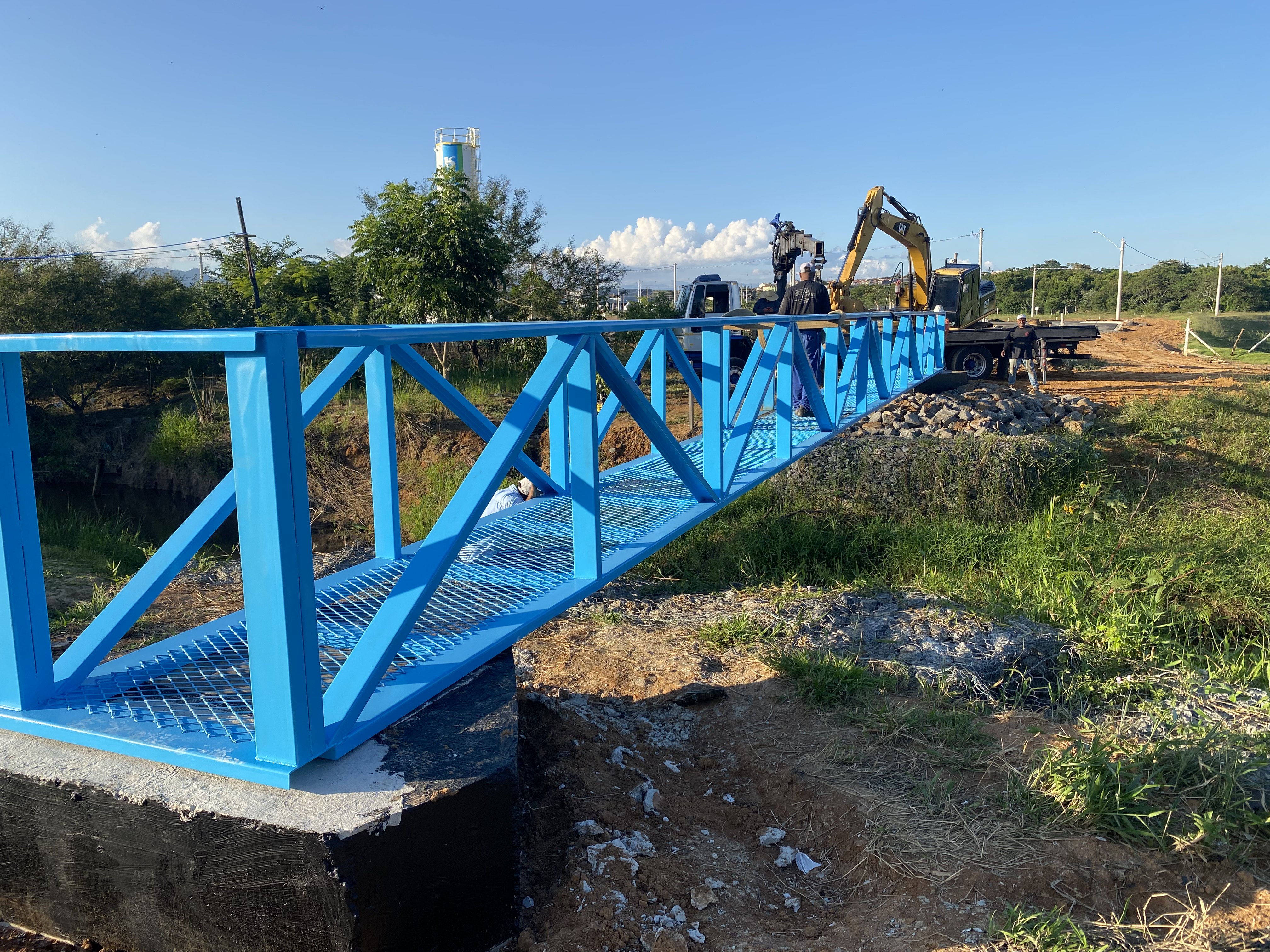 Passarela metálica azul instalada sobre córrego